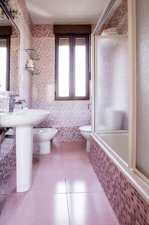 A bathroom with a sink, toilet, and shower area, featuring pink tiled walls and floor. - Apartamentos Casa de la Lonja (Granada)
