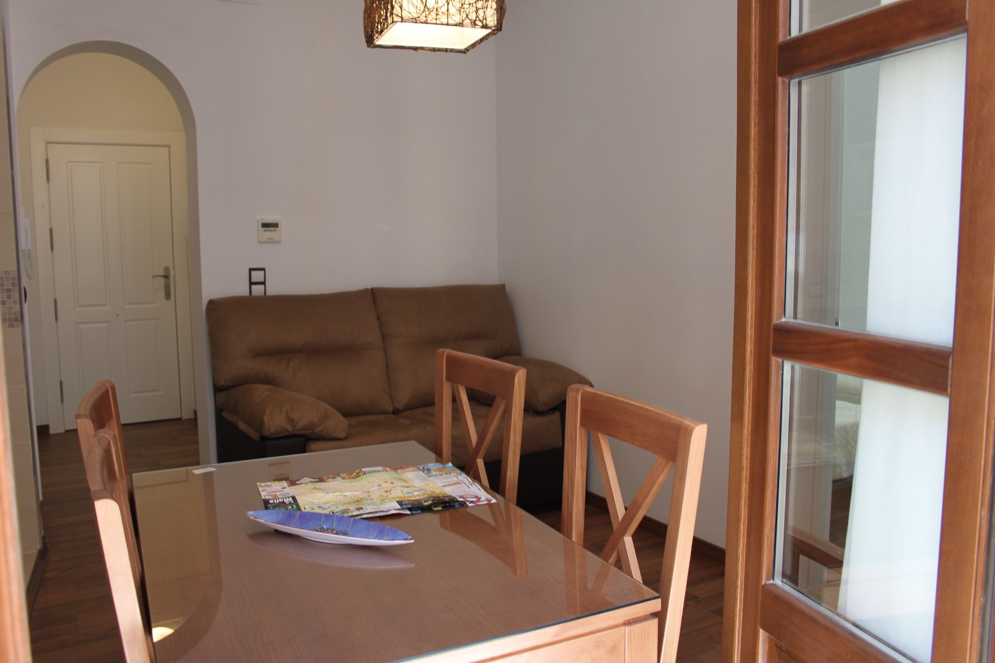 A room with a glass-top dining table, wooden chairs, a brown sofa, and a door with a glass panel.