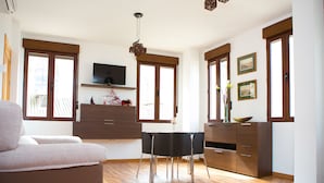 A modern living room with a sofa, a dining table, and a TV mounted on the wall. - Apartamentos Casa de la Lonja (Granada)