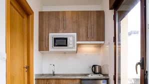 A compact kitchen with wooden cabinets, a stainless steel refrigerator, a microwave, and a sink. - Apartamentos Casa de la Lonja (Granada)