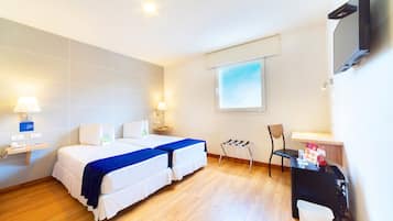 A hotel room with two beds, a desk, a chair, a TV, and a window.