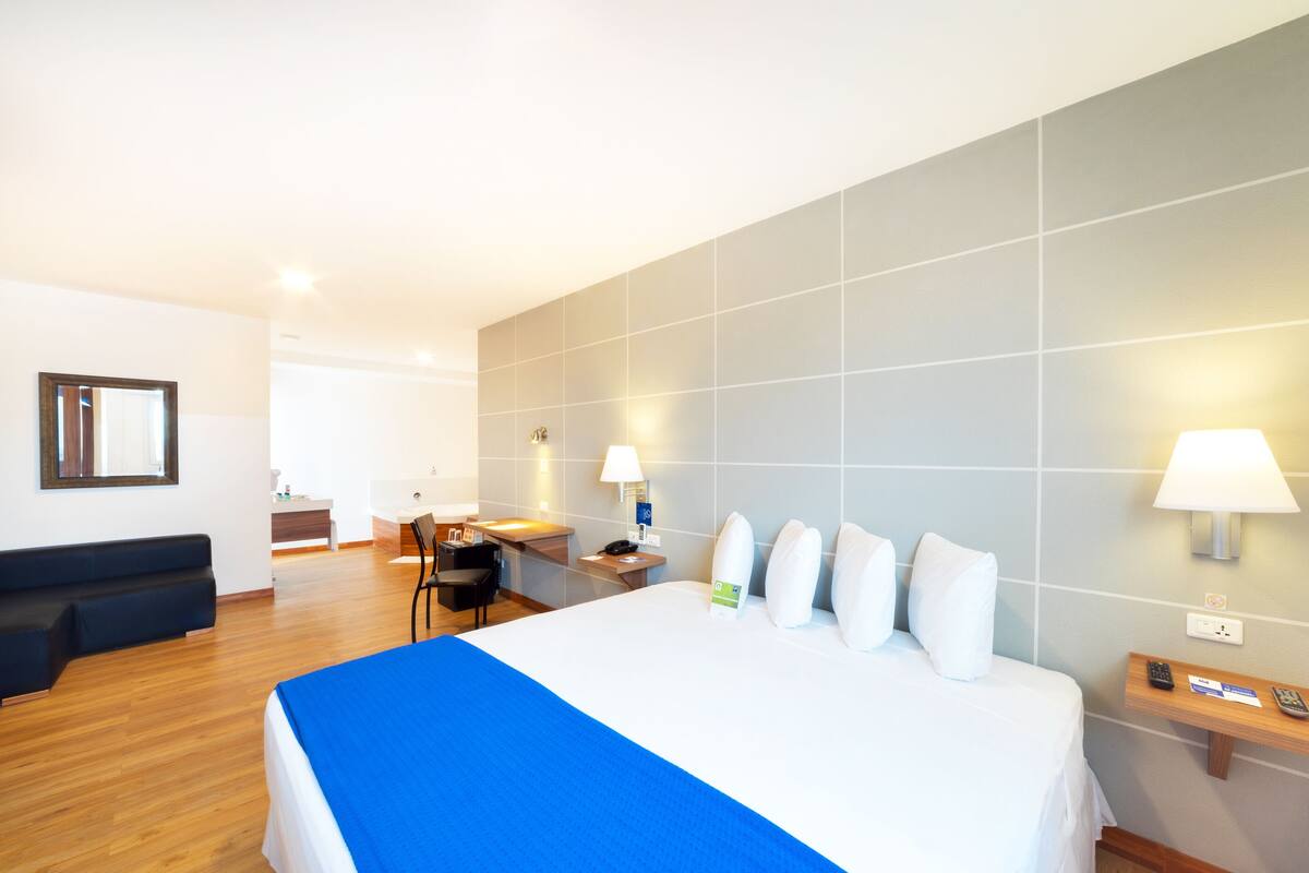 A hotel room with a bed, a desk, a chair, a sofa, and a lamp.