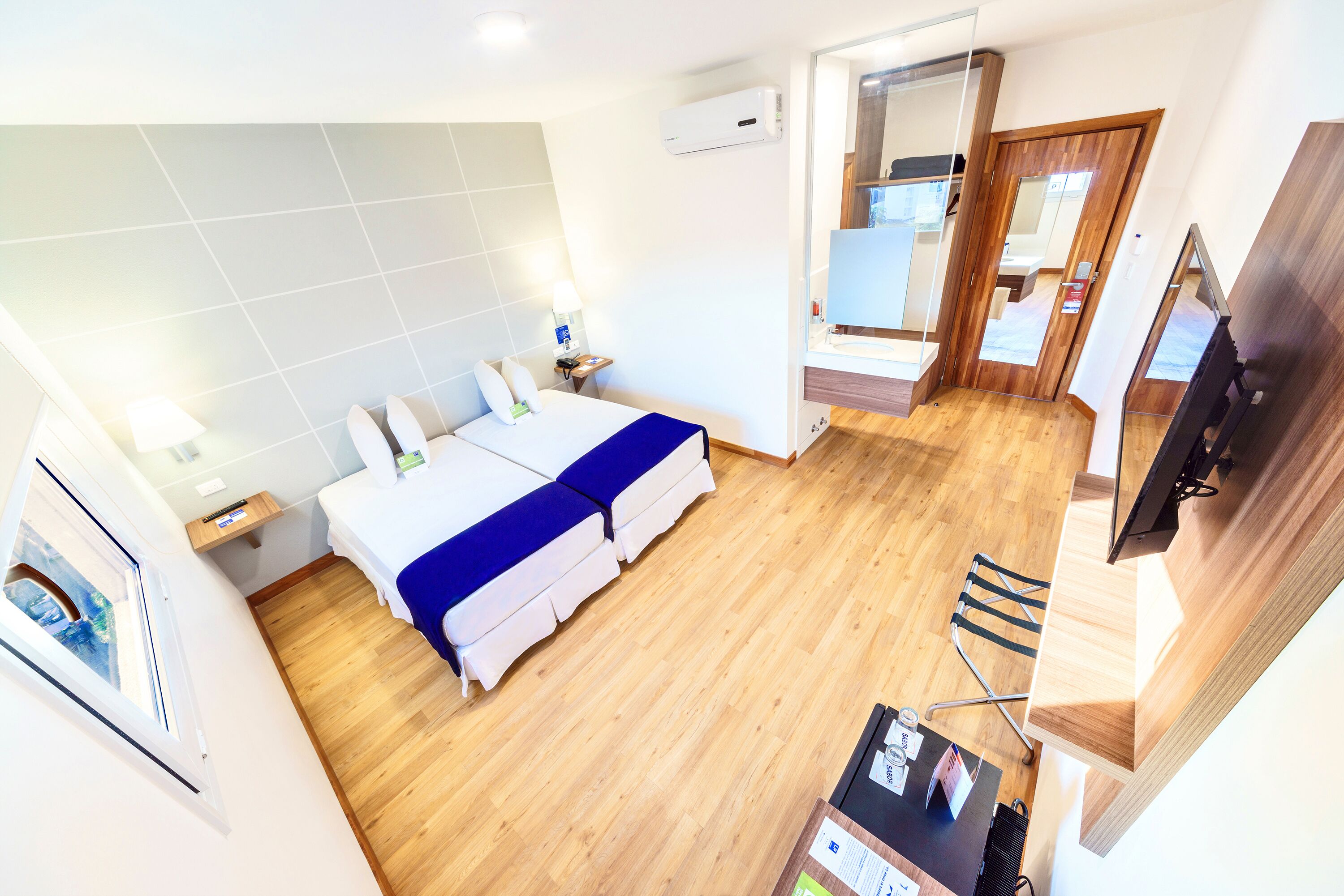 Ein modernes Hotelzimmer mit einem großen Bett, einem Schreibtisch, einem Spiegel und einem Fernseher.