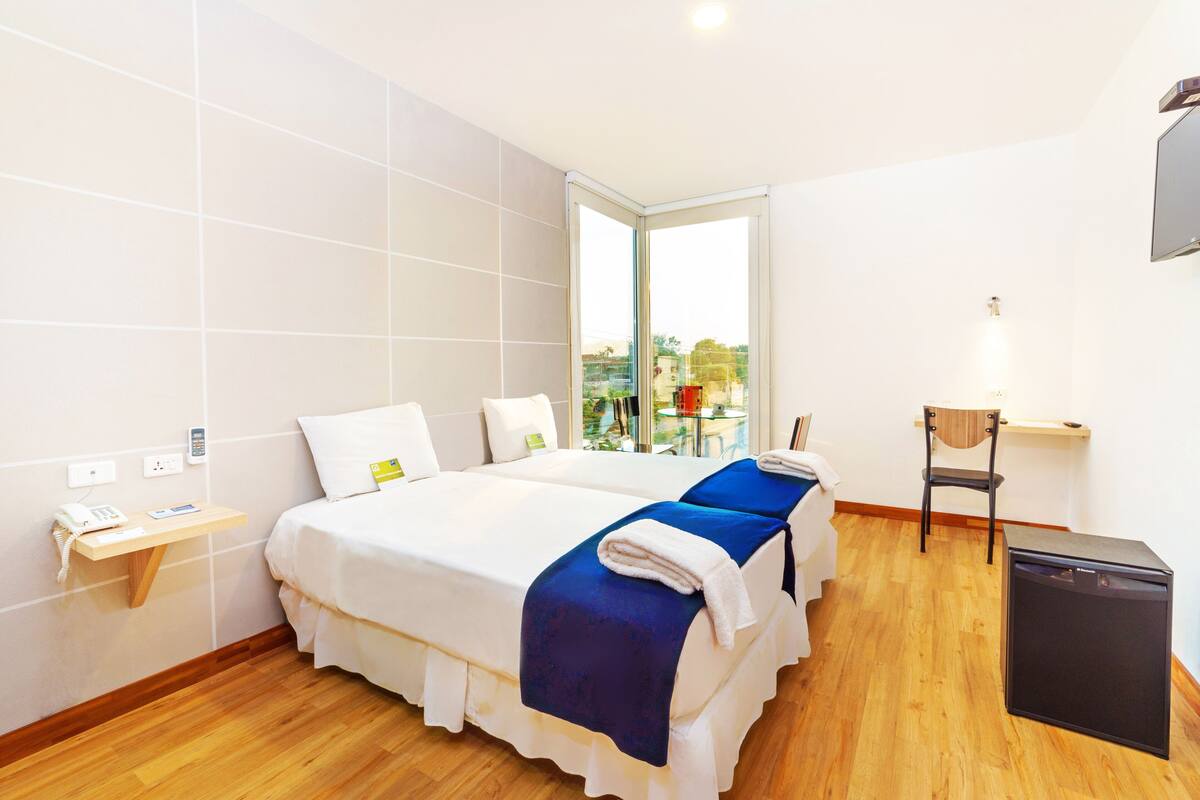 A hotel room with two beds, a desk, a chair, and a small table.