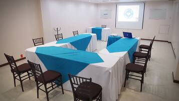 A conference room with tables covered in blue and white tablecloths, equipped with laptops and chairs.