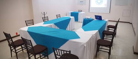 A conference room with tables covered in blue and white tablecloths, equipped with laptops and chairs.