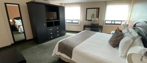 Une chambre d’hôtel avec un lit, un bureau, une armoire et un miroir.