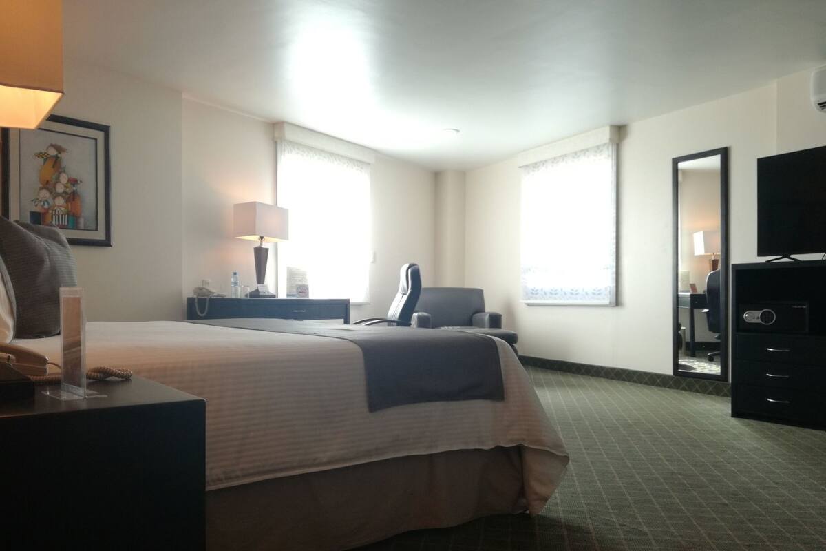 Habitación de hotel con cama, escritorio con lámpara, una silla, televisor y cómoda.