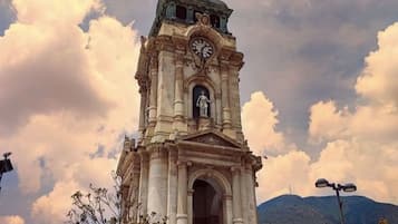 A historic clock tower with a statue at its base, surrounded by a plaza with trees and people.