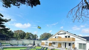 Un edificio moderno con una bandera, un césped y mobiliario para exteriores.