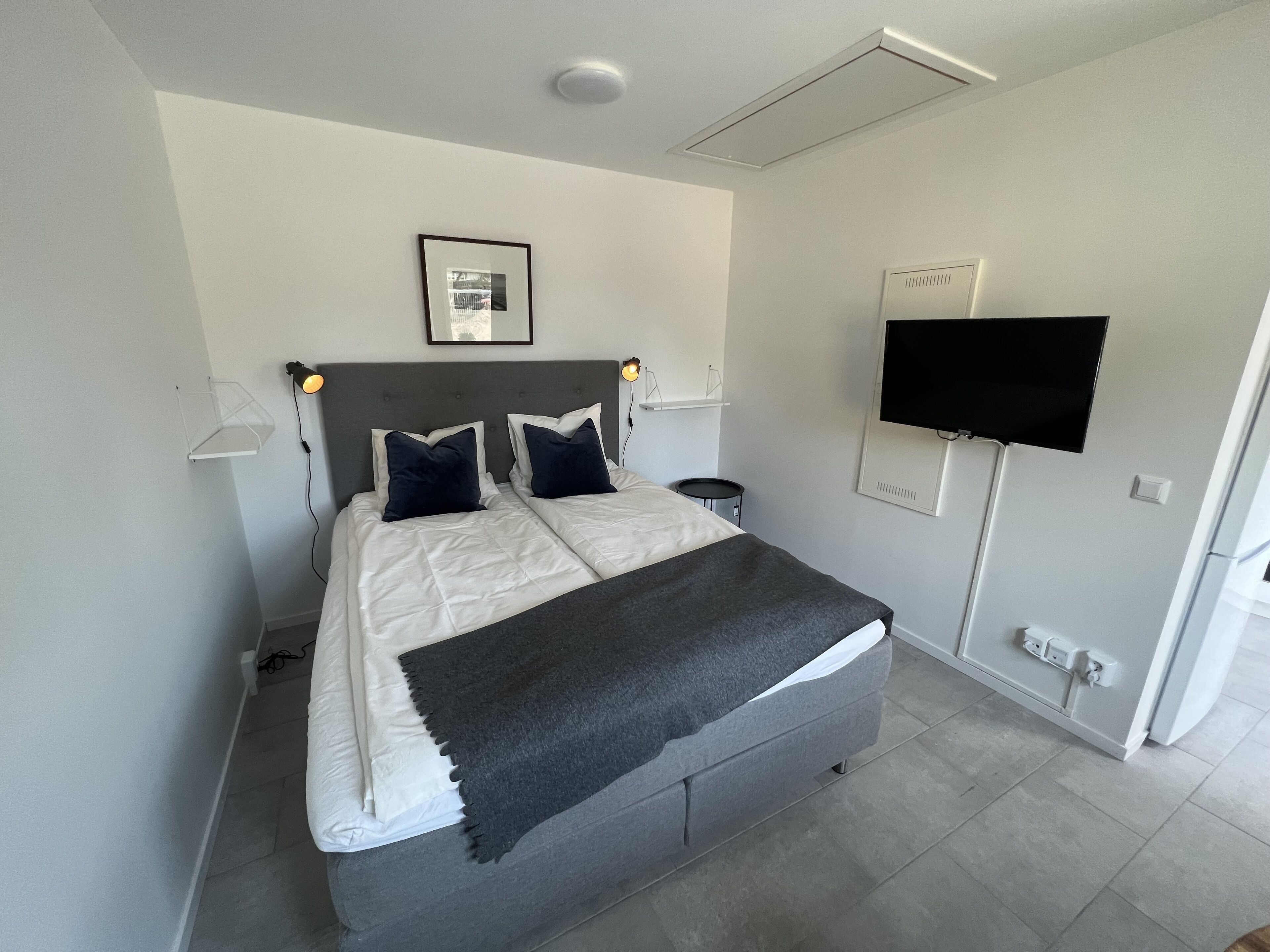 Una camera da letto moderna con un letto, comodini, una TV a schermo piatto e un quadro appeso al muro.