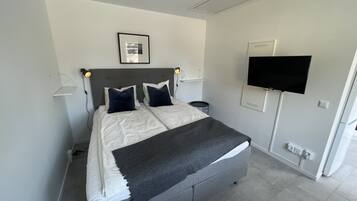 A modern bedroom with a bed, bedside tables, a flat-screen TV, and a framed picture on the wall.