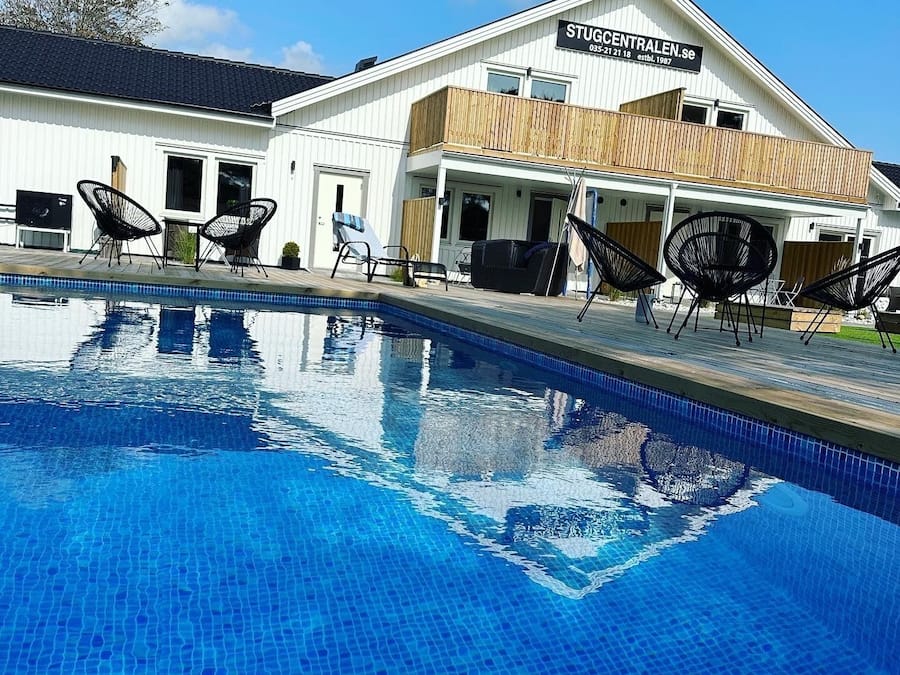 Una piscina con sillones de descanso y un edificio con la leyenda "STUGCENTRALEN.SE" al fondo.