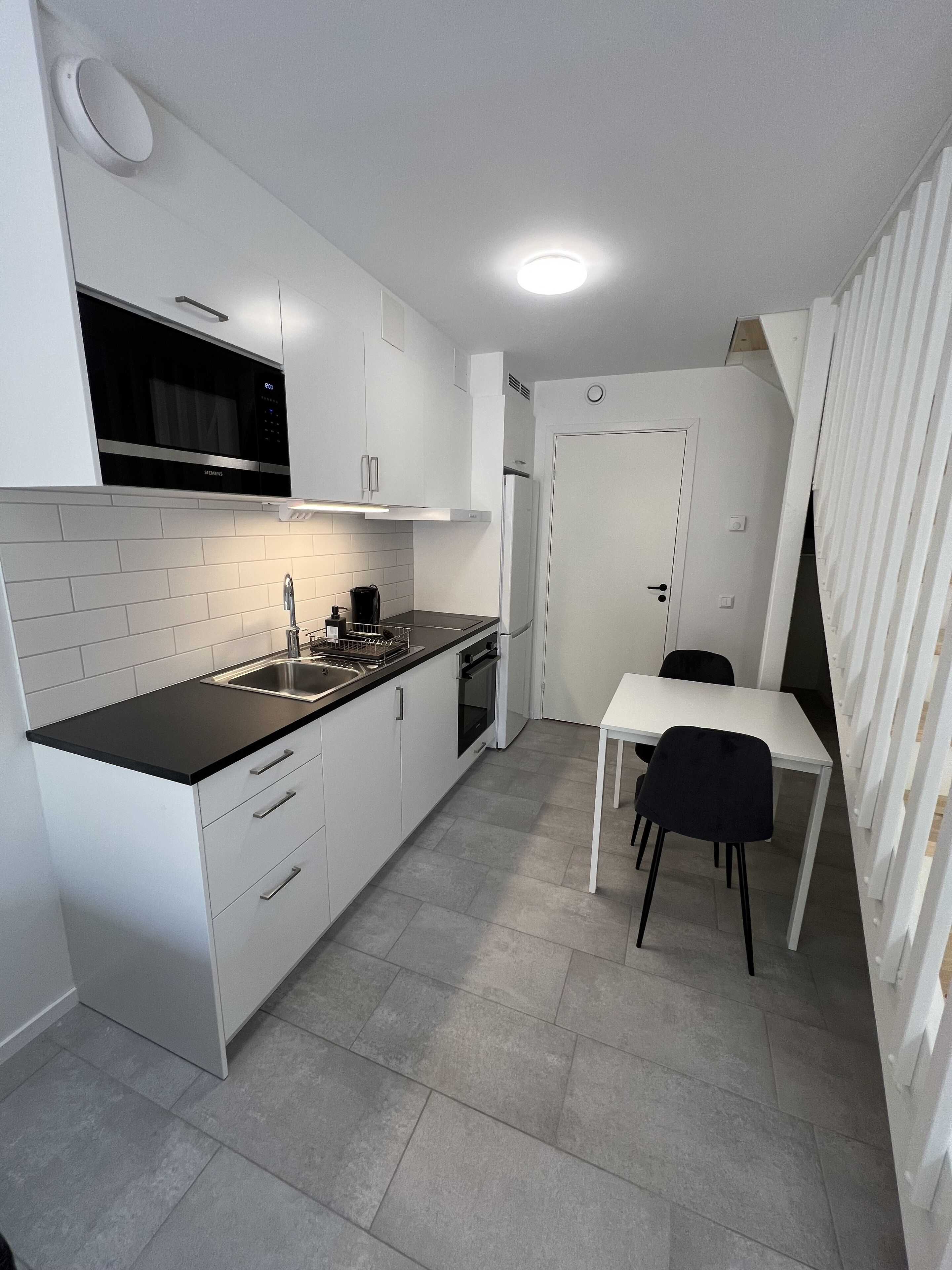 A compact kitchen with white cabinetry, a black countertop, a built-in oven, and a microwave. There's a small dining area with a table and two chairs.