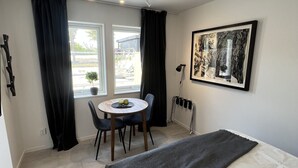 Un dormitorio moderno con cama, una mesa de comedor con sillas, una ventana con cortinas y una obra de arte enmarcada en la pared.