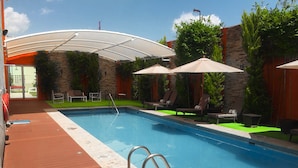 Ein Schwimmbecken mit Holzterrasse, Liegestühlen und Sonnenschirmen.