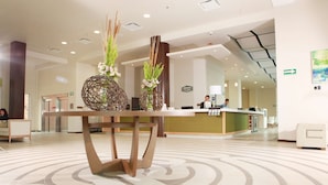 Eine moderne Hotelhalle mit einer Rezeption, dekorativen Vasen und einem gemusterten Boden.