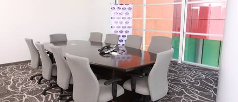 A conference room with a glass table, grey chairs, a carpeted floor, and a window with colorful panels.