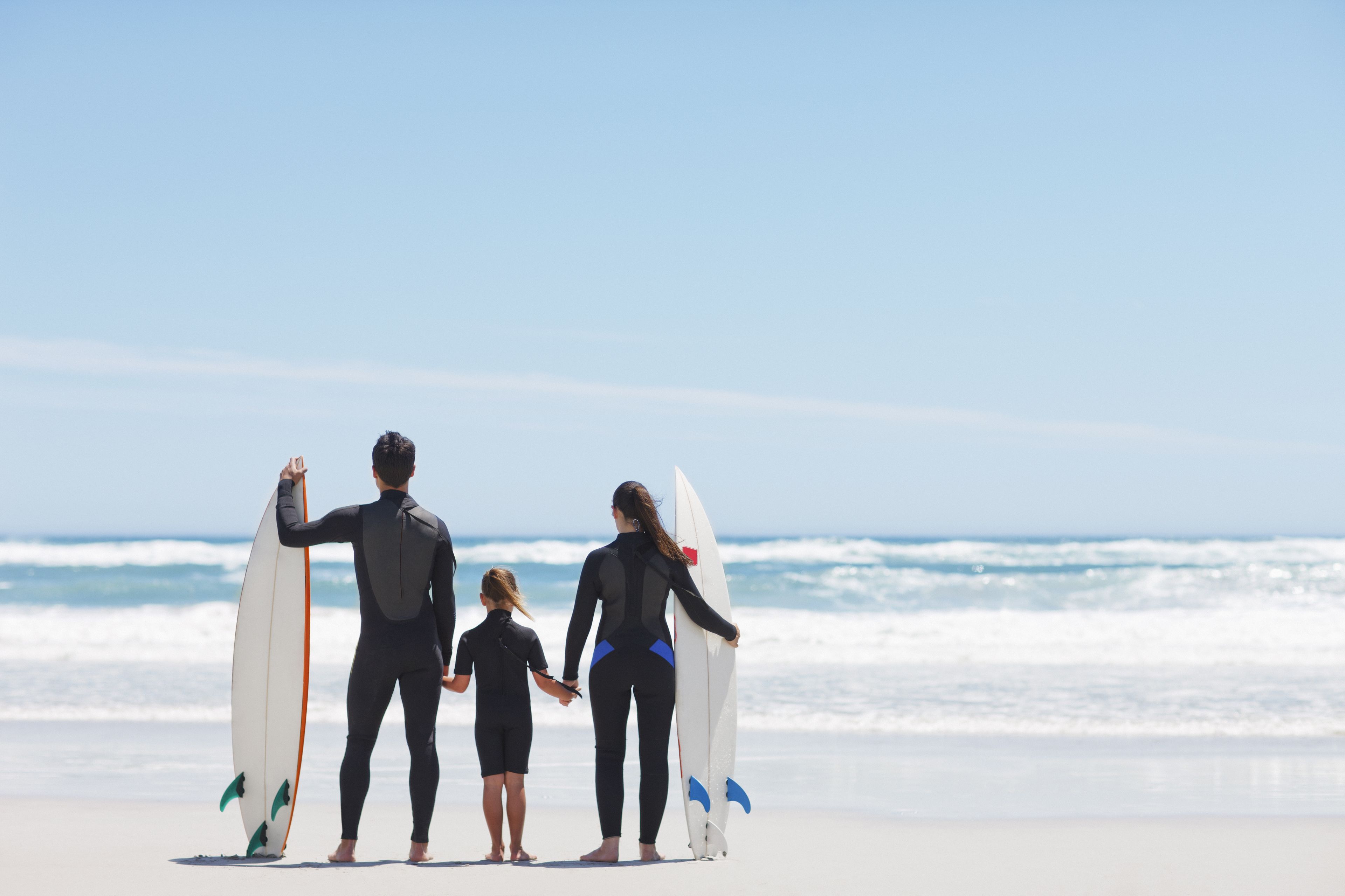 Tres personas sostienen tablas de surf en la playa.