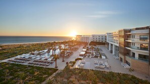 Un resort con zona de piscina, tumbonas y vista al océano al atardecer.