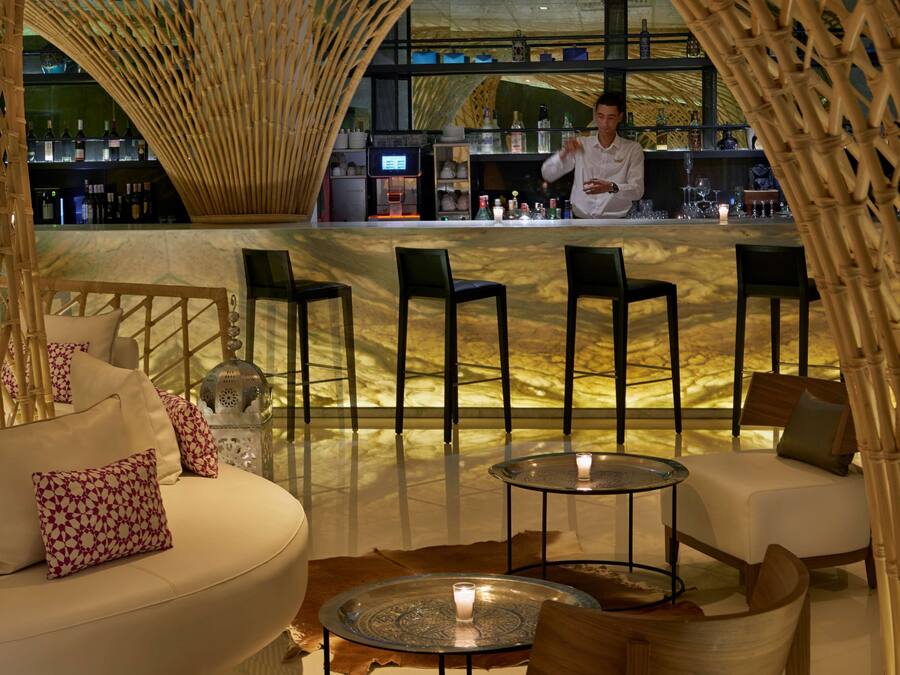 Zona de bar con arco de bambú, asientos con cojines y barra con botellas.