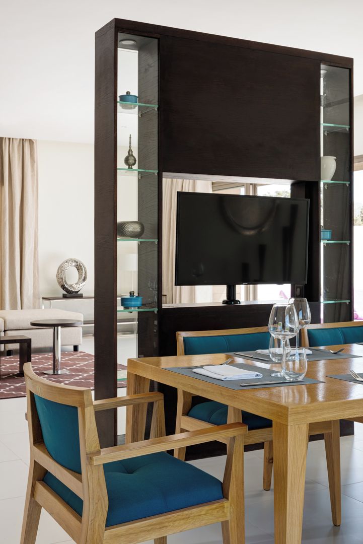 A modern dining area with a wooden table, blue cushioned chairs, and a large flat-screen TV.