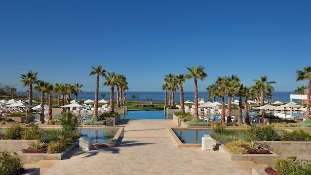 Un resort con piscina, palmeras y sombrillas de playa.