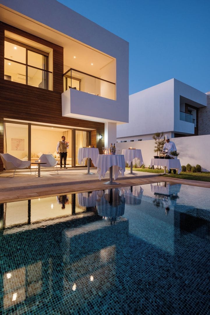 Un hotel moderno con piscina, asientos al aire libre y un chef preparando comida.