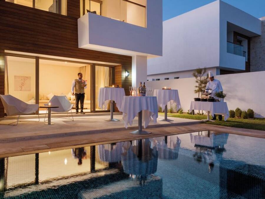 Un hotel moderno con piscina, asientos al aire libre y un chef preparando comida.