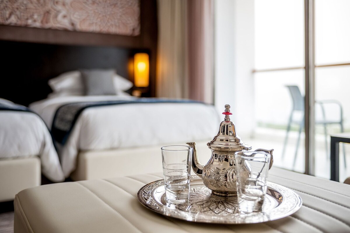 A hotel room with a bed, bedside table, and a tray with a teapot and glasses.