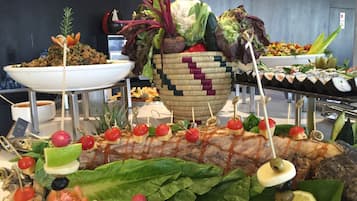 Un bufé con diversos alimentos, incluyendo brochetas, ensaladas y un gran pez como pieza central.