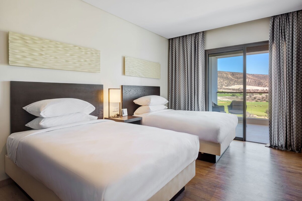 A hotel room with two beds, a large window with a view, and a modern design.