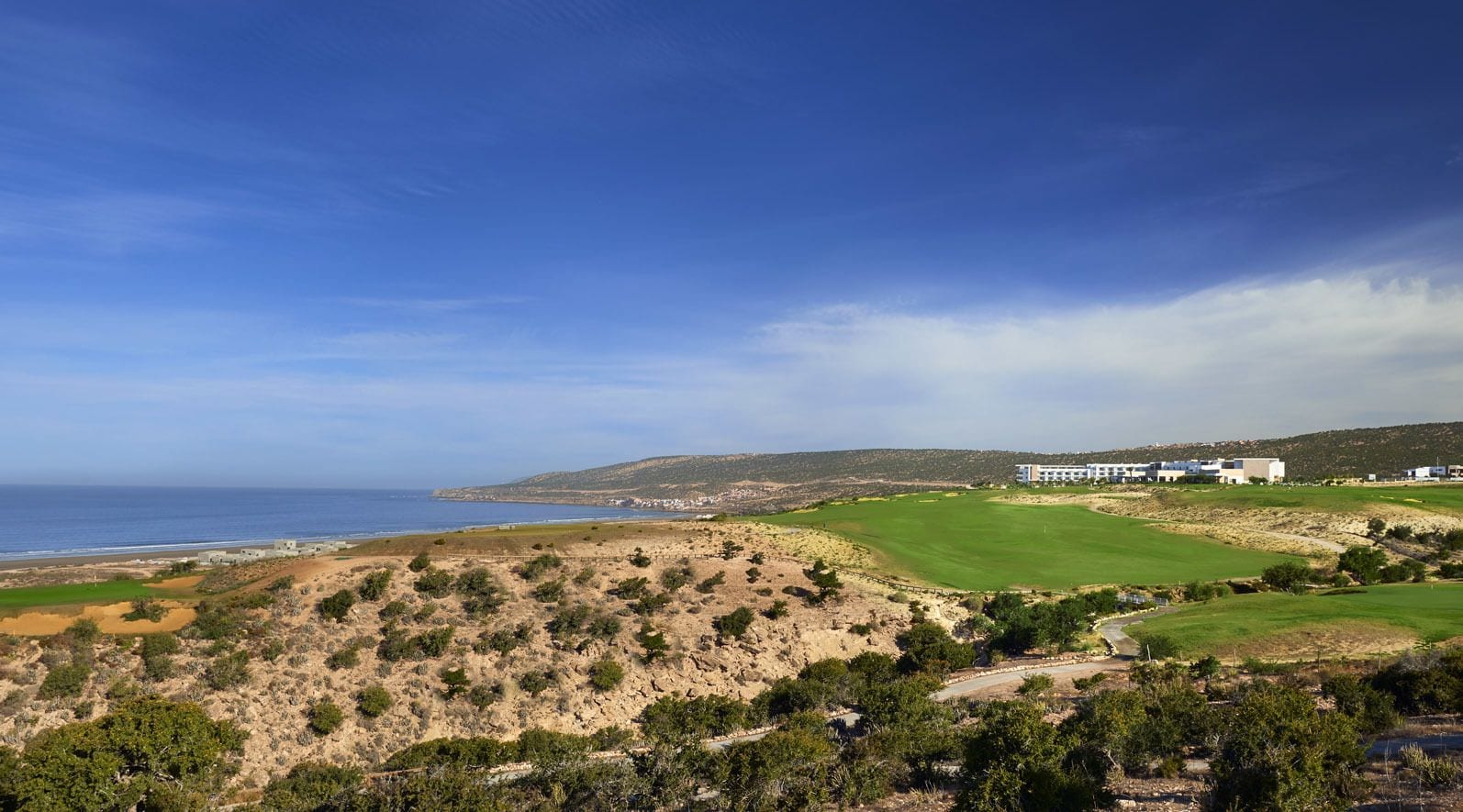 A coastal landscape with a golf course, buildings, and a view of the sea.