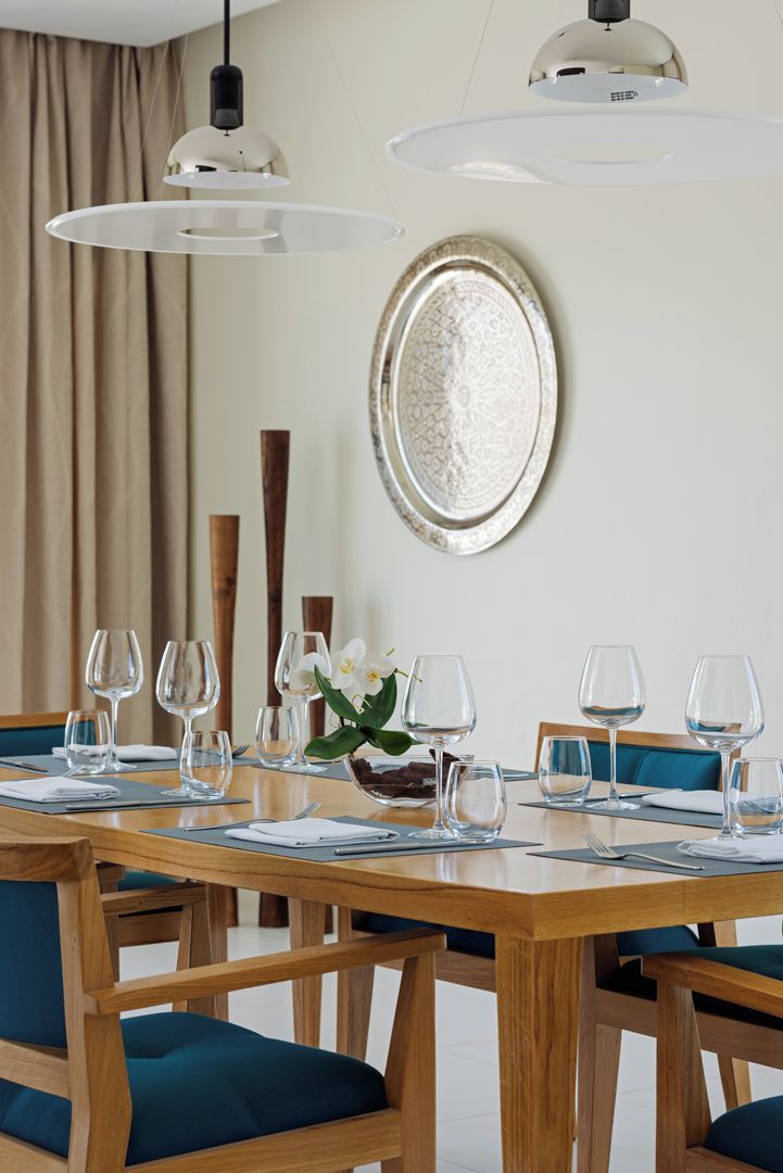 Un comedor con una mesa de madera lista para una comida, rodeada de sillas con cojines color turquesa.