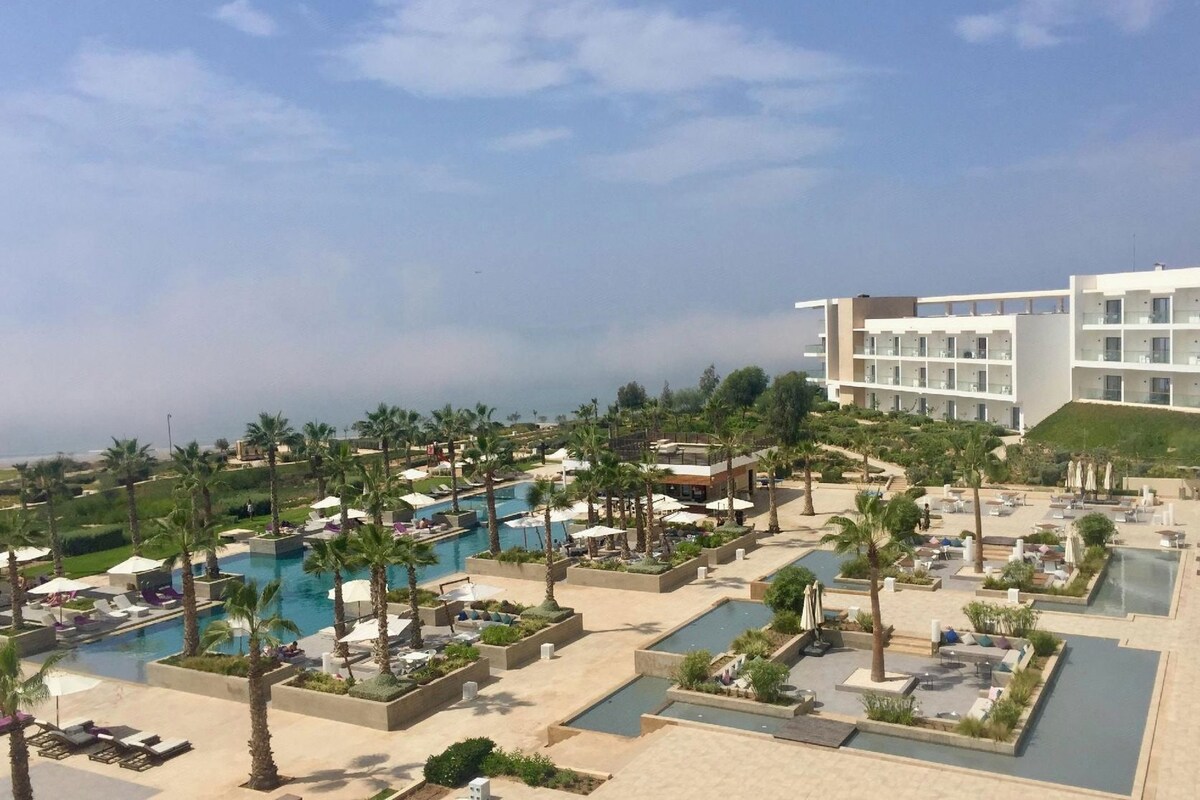 A resort with multiple swimming pools, palm trees, and a large building with balconies.