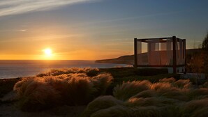Una estructura moderna de vidrio con vista al atardecer sobre el océano.