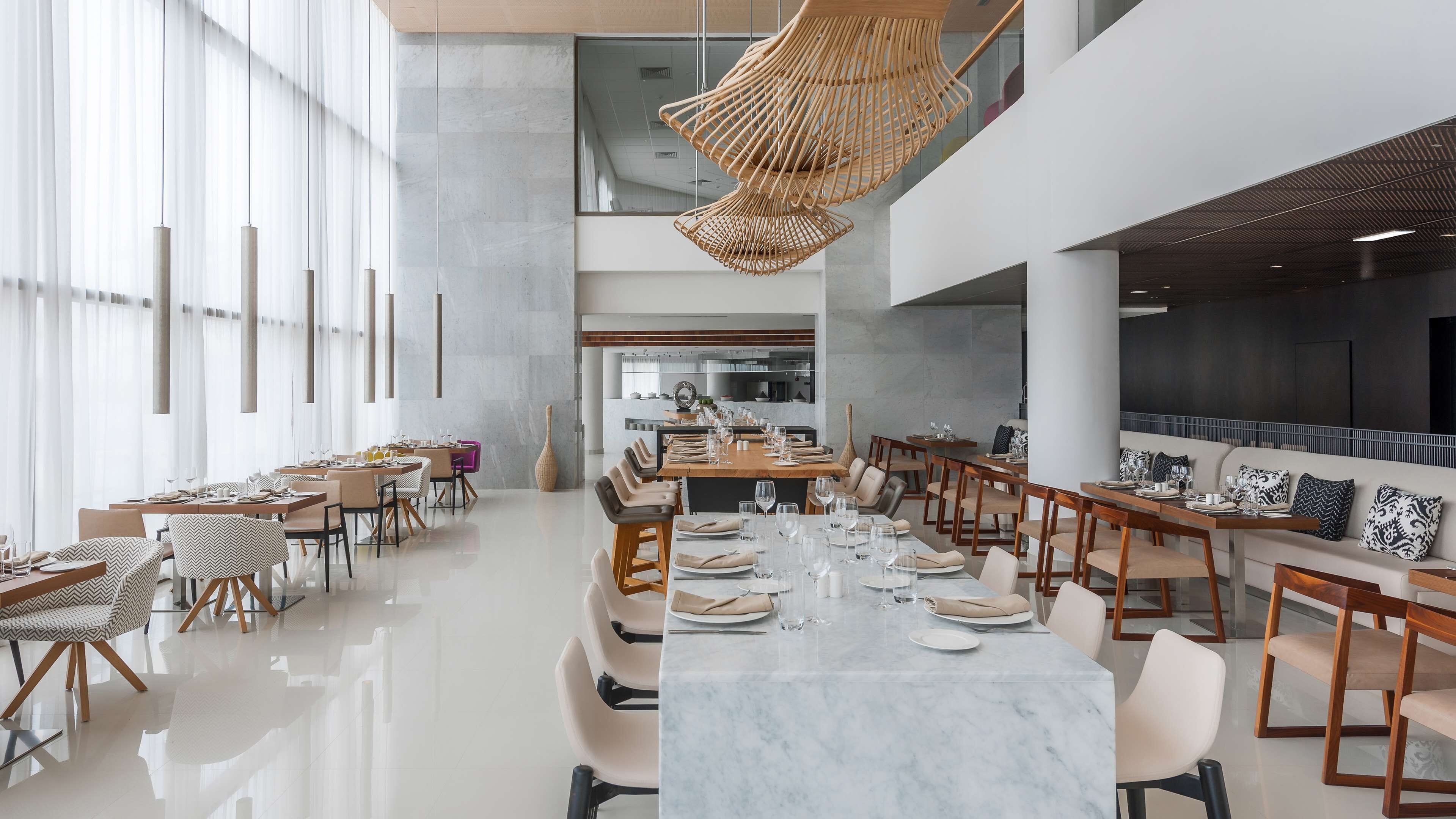 A modern dining area with marble tables, leather chairs, and a central island with a kitchen in the background.