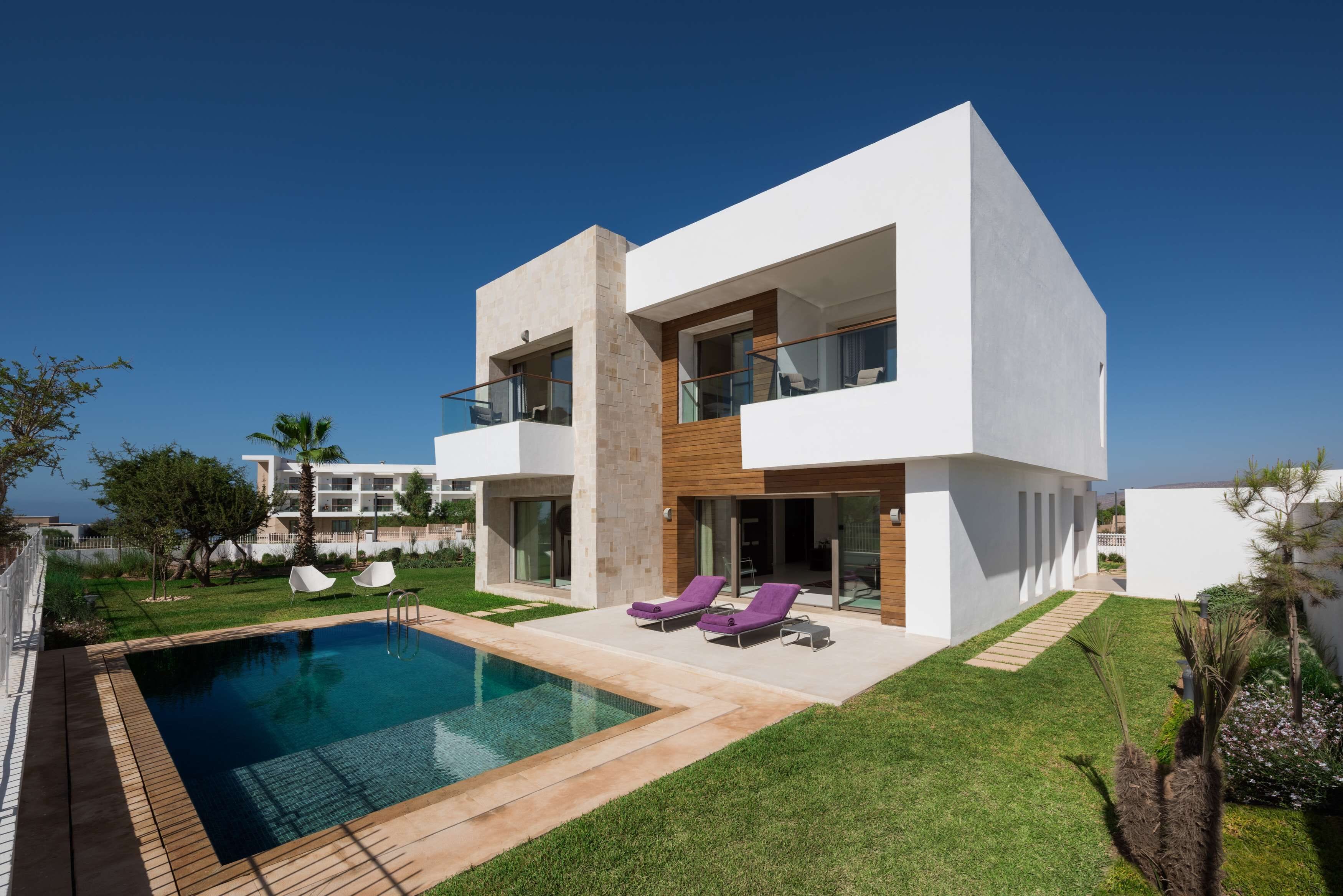 Uma casa moderna com dois andares, piscina, varanda com cadeiras de descanso e gramado bem cuidado.