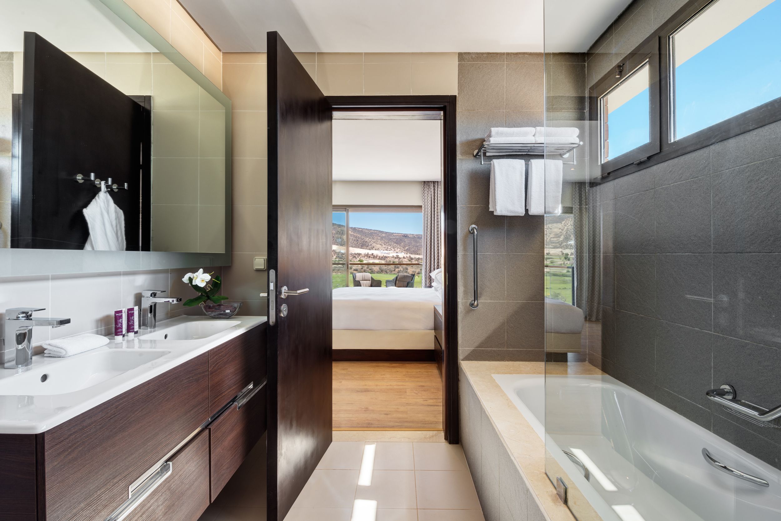 A modern bathroom with a large mirror, two sinks, a bathtub, and a shower.