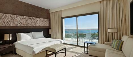 A hotel room with a large bed, a sofa, a small table, and a view of the ocean.