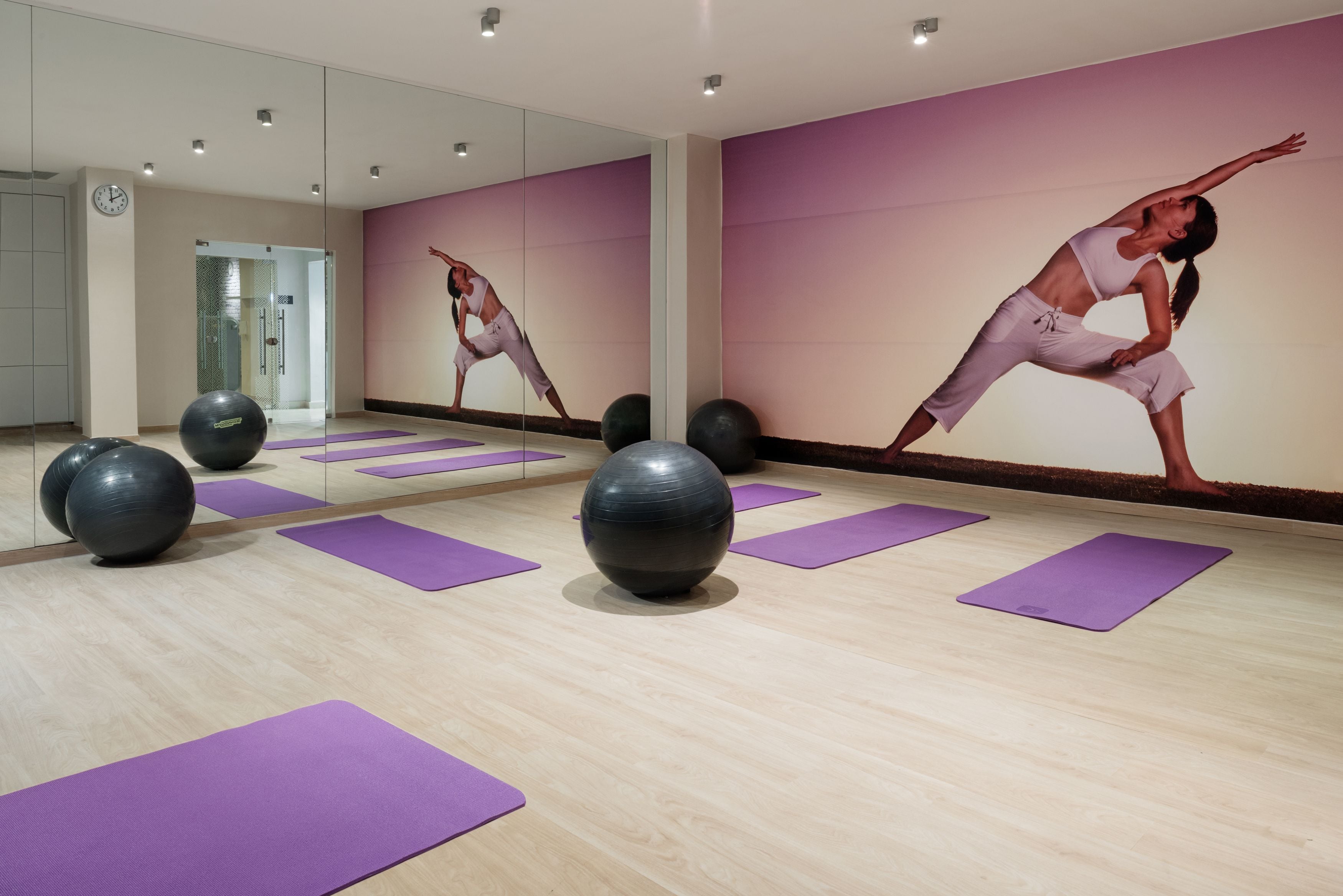 Ett gym med lila träningsmattor, träningsbollar och en vägg täckt med speglar.