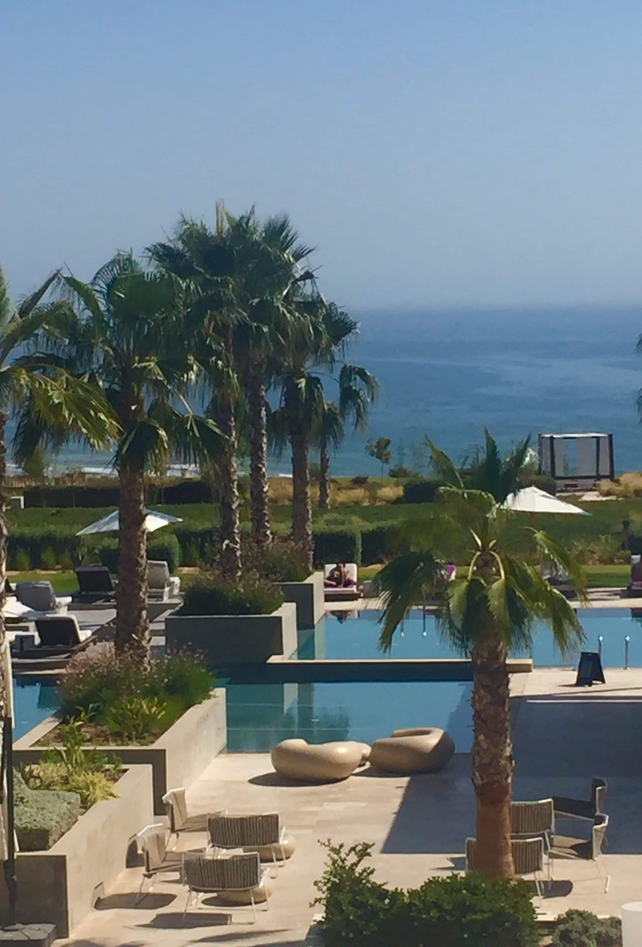 A poolside area with lounge chairs, palm trees, and a view of the ocean.