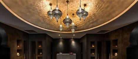 A modern interior with a central marble altar, ornate hanging chandeliers, and recessed lighting in dark walls.