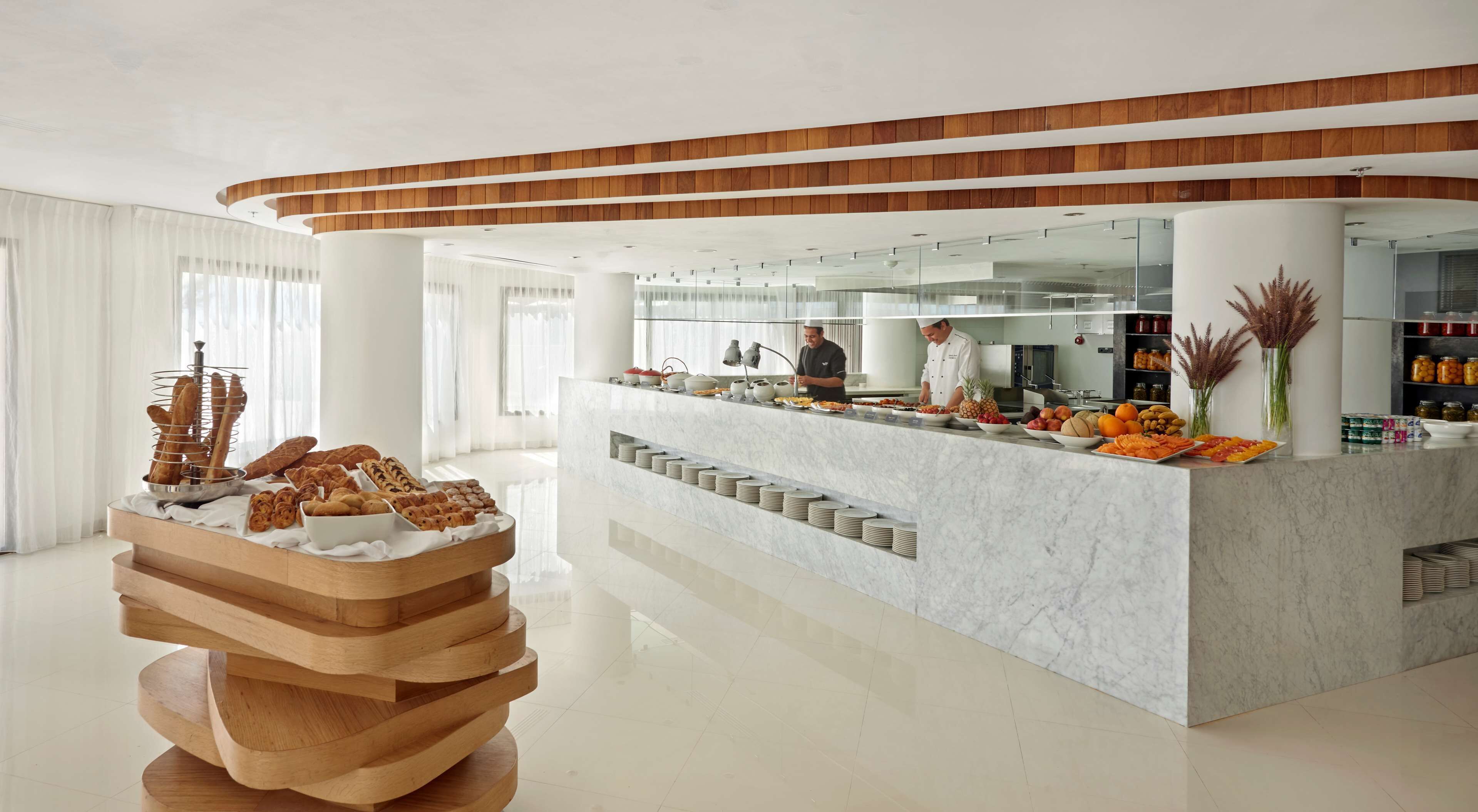 A modern hotel lobby with a marble reception desk, a wooden sculpture, and a buffet area.
