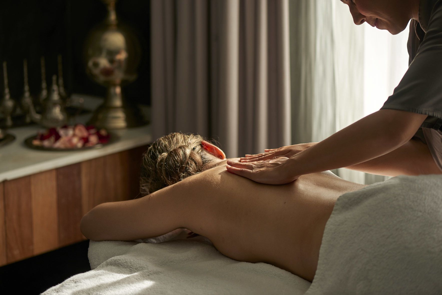 A massage therapy session in a room with a wooden massage table, a white towel, and a decorative lamp in the background.