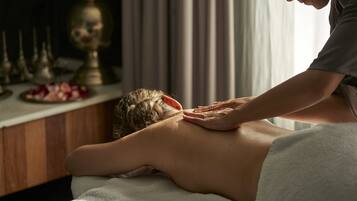 A massage therapy session in a room with a wooden massage table, a white towel, and a decorative lamp in the background.