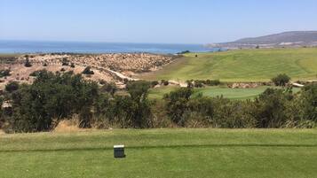 A golf course with a clear view of the ocean and distant hills.