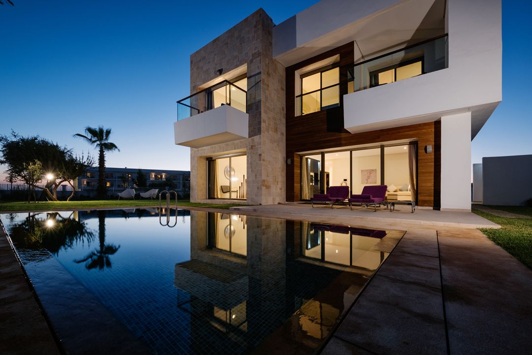 A modern two-story house with a swimming pool, large windows, and outdoor seating.