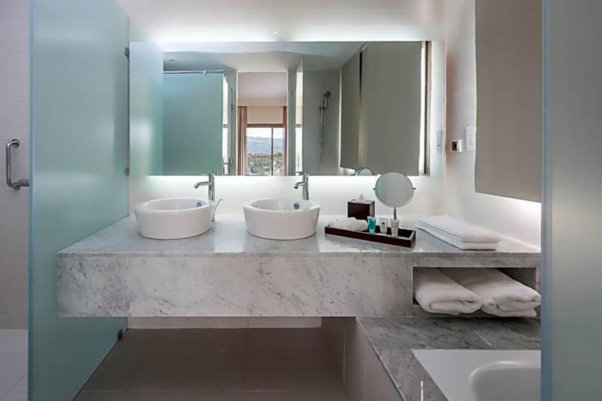 A modern bathroom with two sinks, a large mirror, and a bathtub.