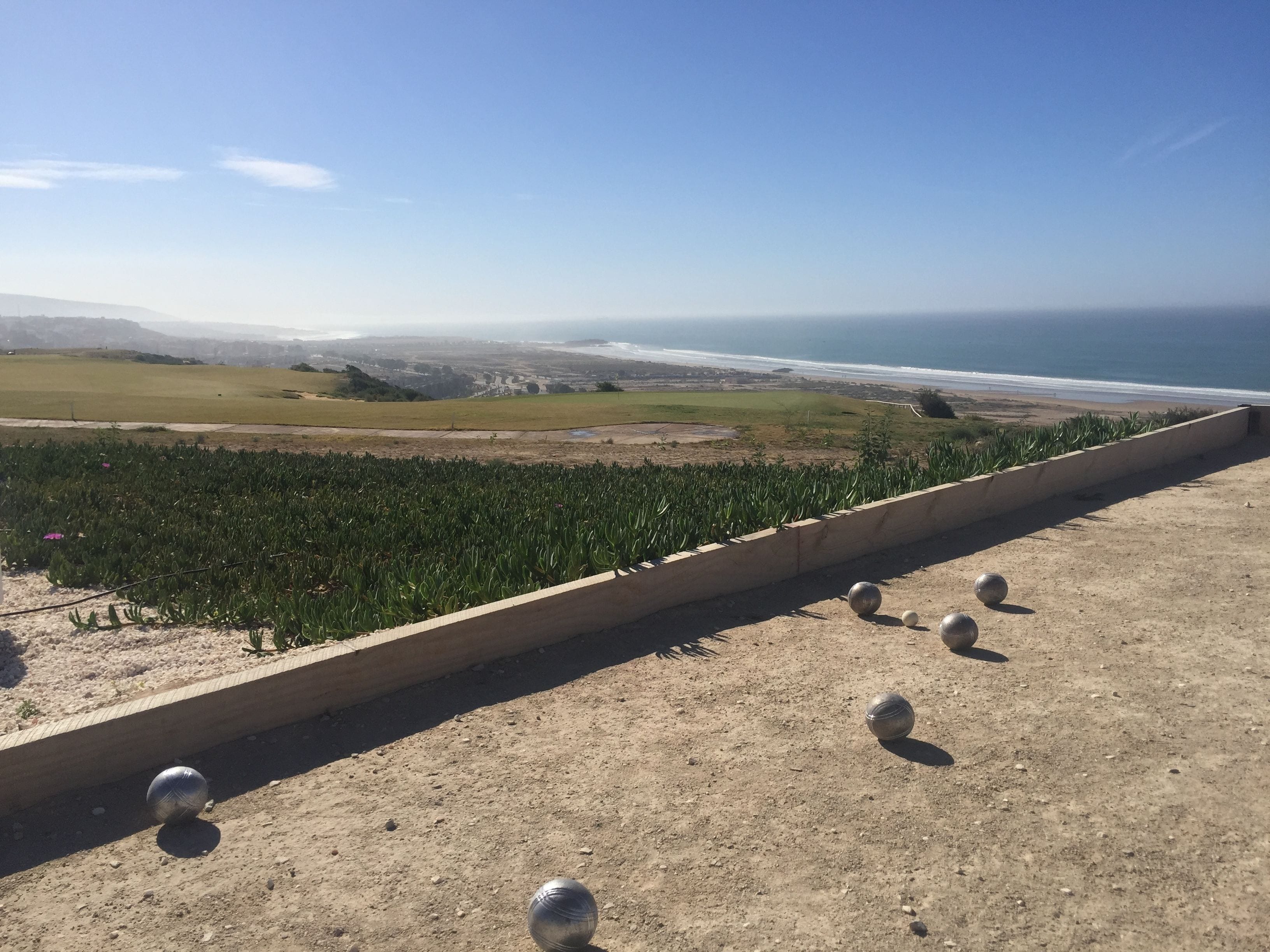 A coastal view with a dirt path and metal spheres, leading to a grassy area and the ocean.